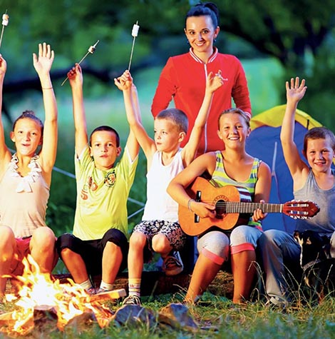 Sütögető gyerekek a tűz körül gitárral és felvigyázó nővel